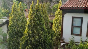 A house with a tiled roof, surrounded by lush greenery and a rocky hillside. - Gönül sefası bütik otel  (Amasya)