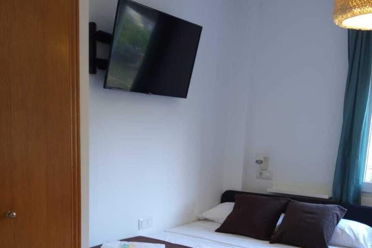 Ett hotellrum med en säng, en tv som är monterad på väggen och ett fönster med gardiner.
