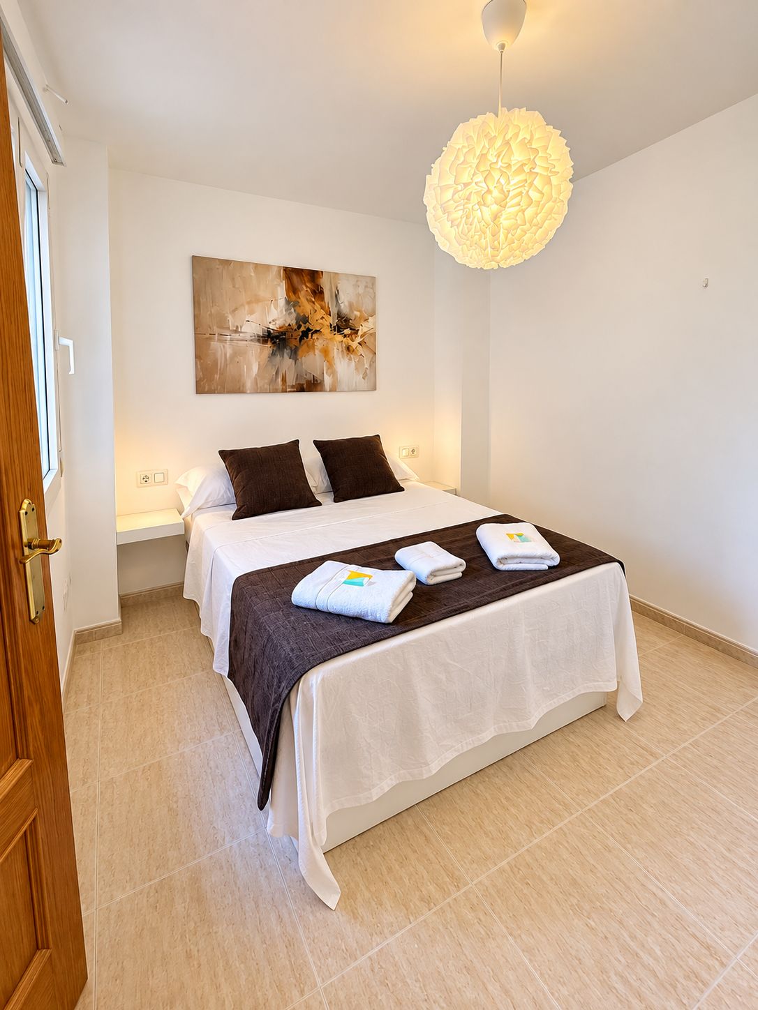 Una habitación de hotel con una cama, un cuadro en la pared y una lámpara colgante.