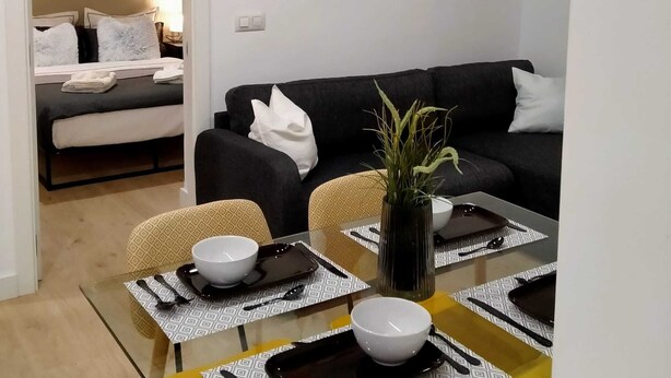 A modern living room with a black sofa, a dining table with placemats, and a large abstract painting on the wall. - RESIDENCIAL ALCOY (Alcoy)