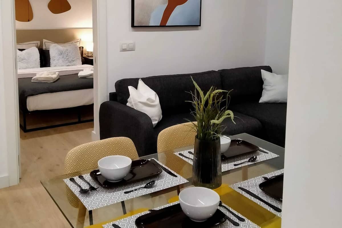 Ett modernt vardagsrum med en svart soffa, ett matbord med underlägg och en stor, abstrakt tavla på väggen.