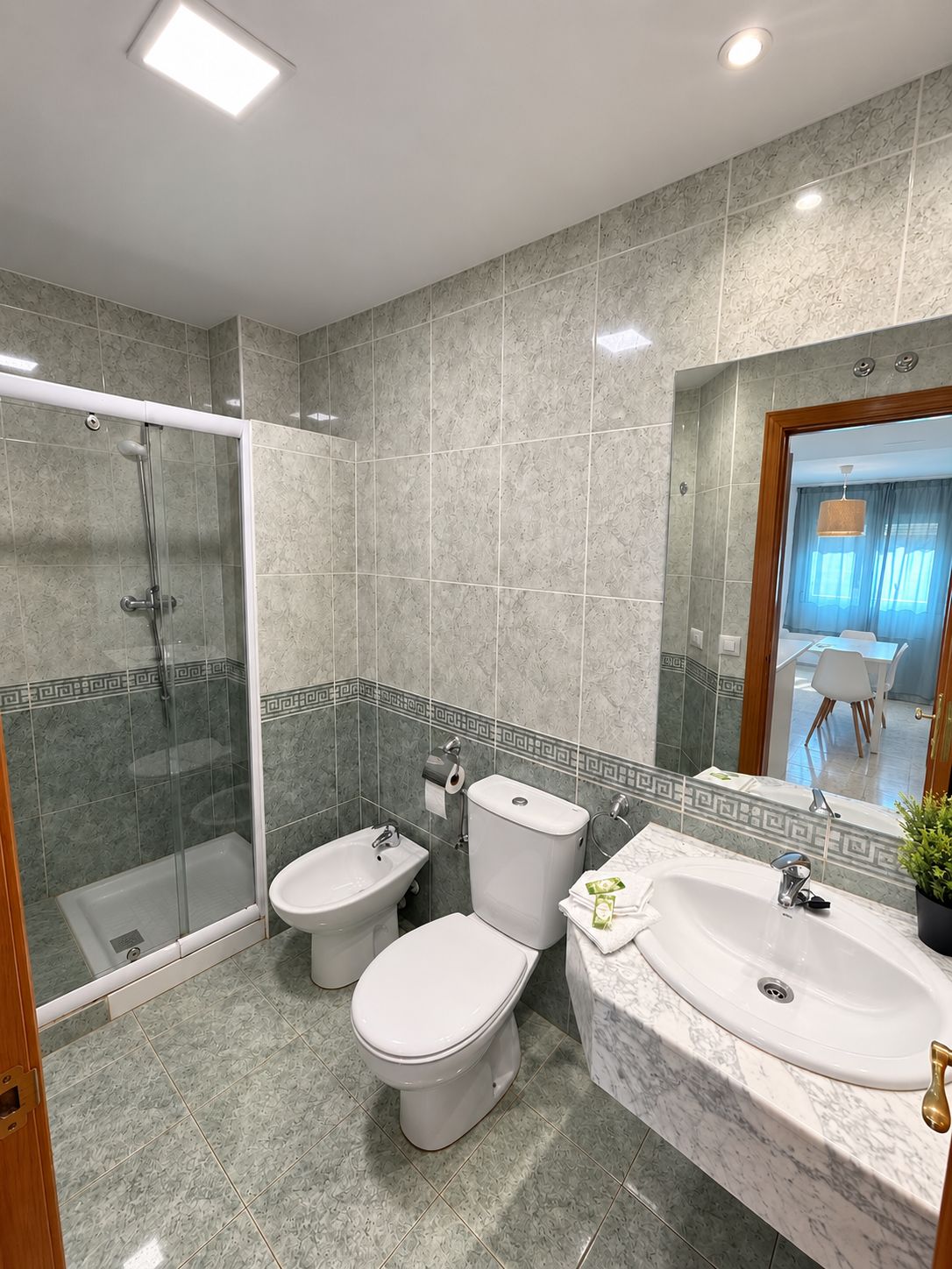 Un baño moderno con ducha envuelta en vidrio, dos inodoros, un lavabo y un espejo.