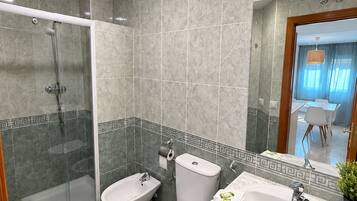 Un baño moderno con ducha envuelta en vidrio, dos inodoros, un lavabo y un espejo.