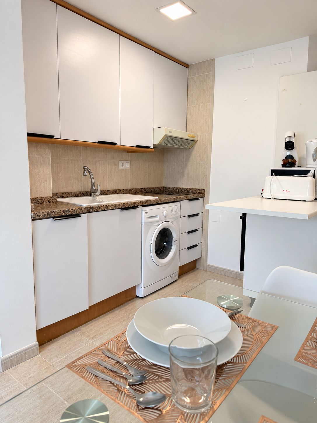 A modern kitchen with a built-in washing machine, a coffee maker, and a toaster on the countertop.
