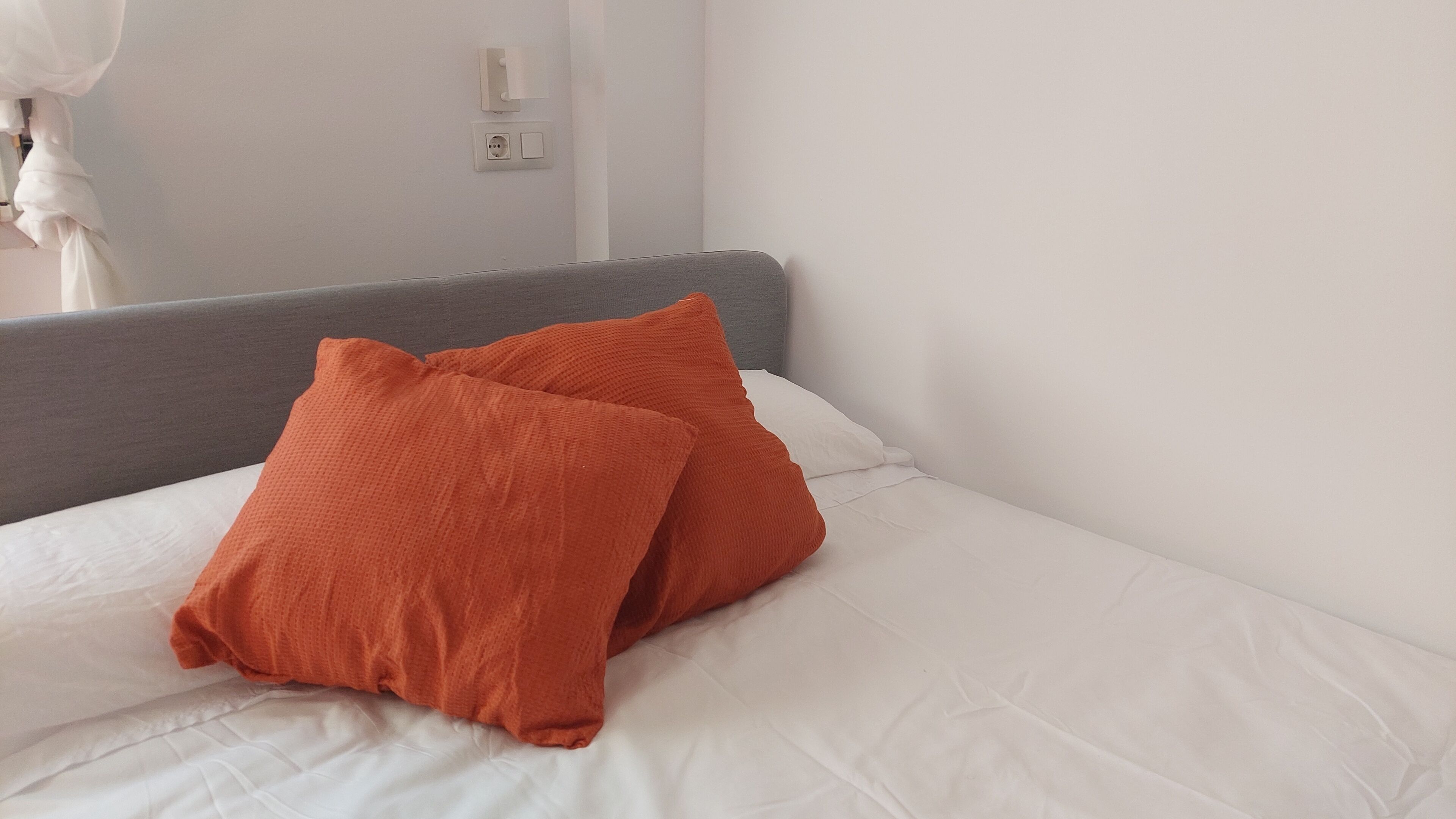 A bed with white bedding and two orange pillows.