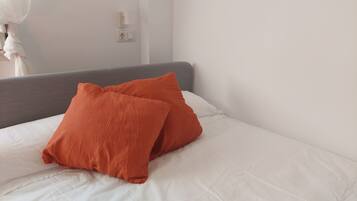 A bed with white bedding and two orange pillows.