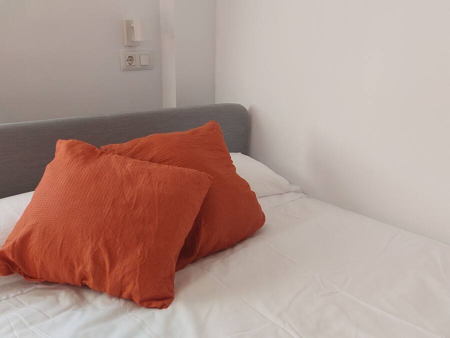 A bed with white bedding and two orange pillows.