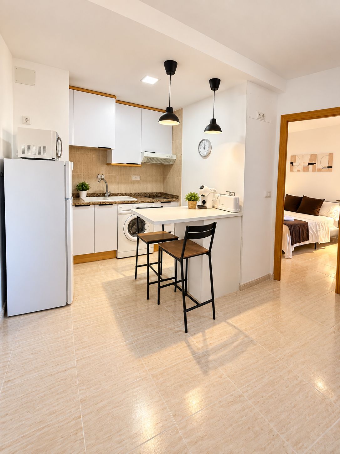 Una cocina moderna con armarios blancos, horno integrado, un lavamanos y una zona de comedor con dos sillas.