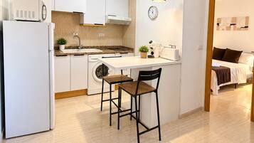 Una cocina moderna con armarios blancos, horno integrado, un lavamanos y una zona de comedor con dos sillas.