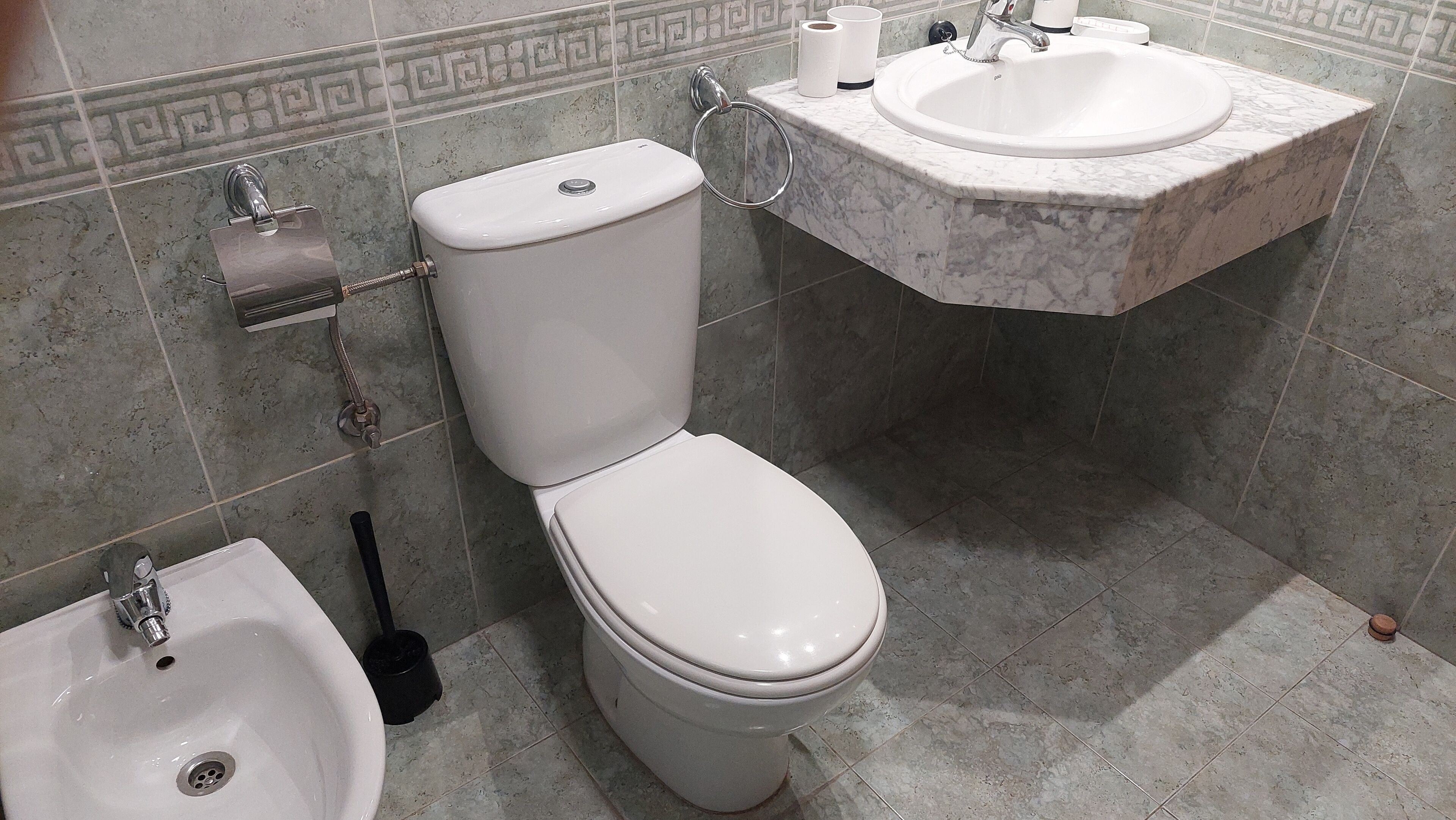 Un baño con inodoro, bidé, lavabo y papel higiénico.