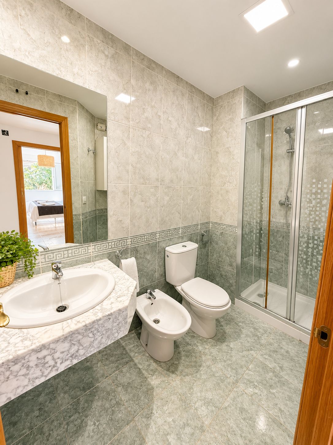 Een badkamer met een marmeren wastafel, twee toiletten, een douchecabine en een grote spiegel.