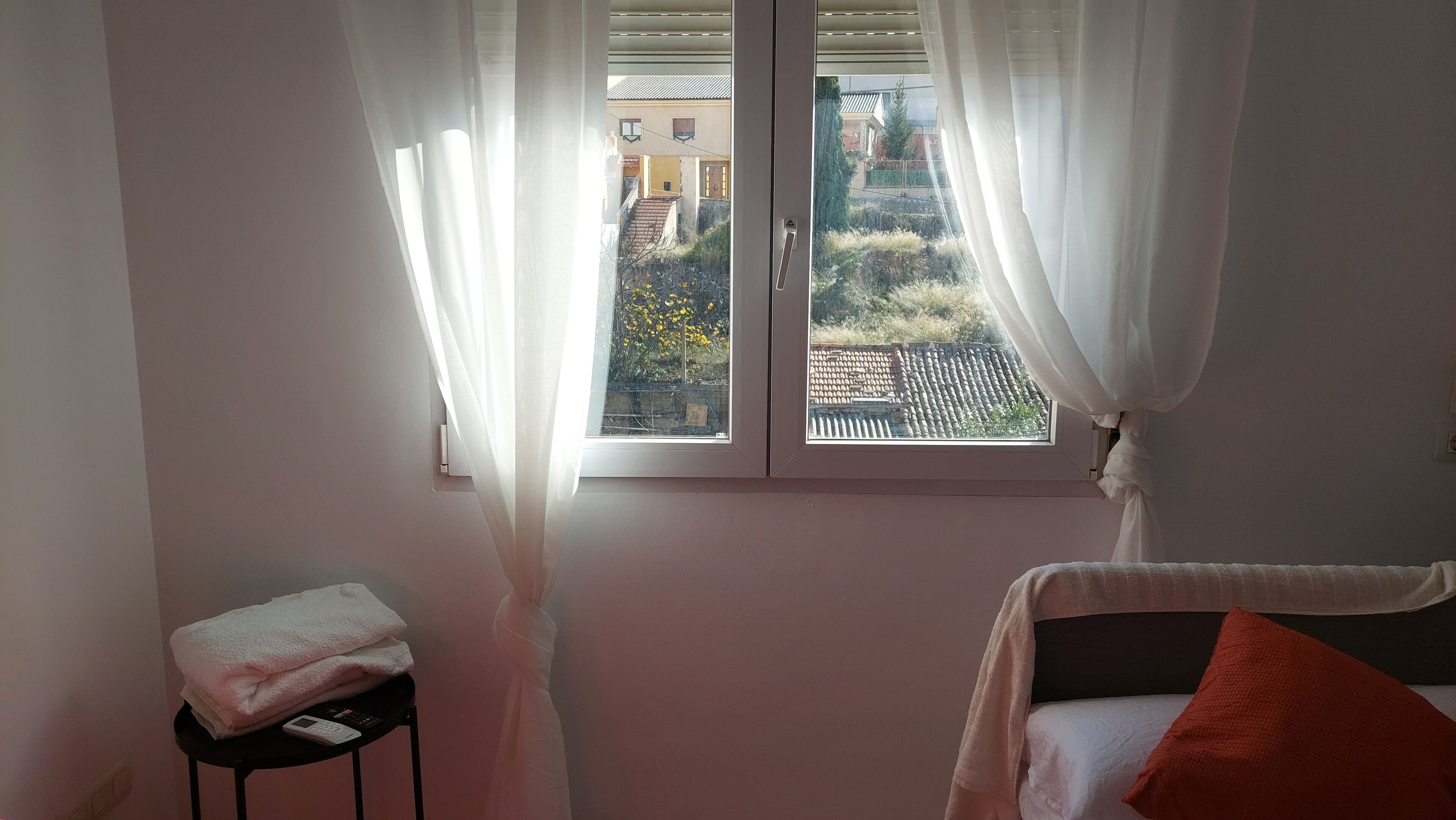 Un dormitorio con ventana, una mesita de noche con una toalla y una cama con almohada.