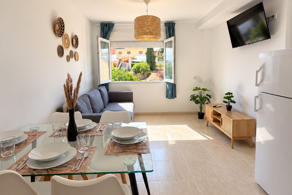 A modern living space with a dining area, a sofa, a TV, and a kitchen area.