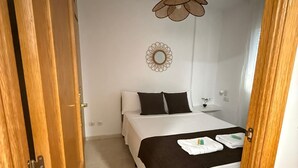 A bedroom with a bed, a hanging light fixture, a wall mirror, and a door. - RESIDENCIAL ALCOY (Alcoy)