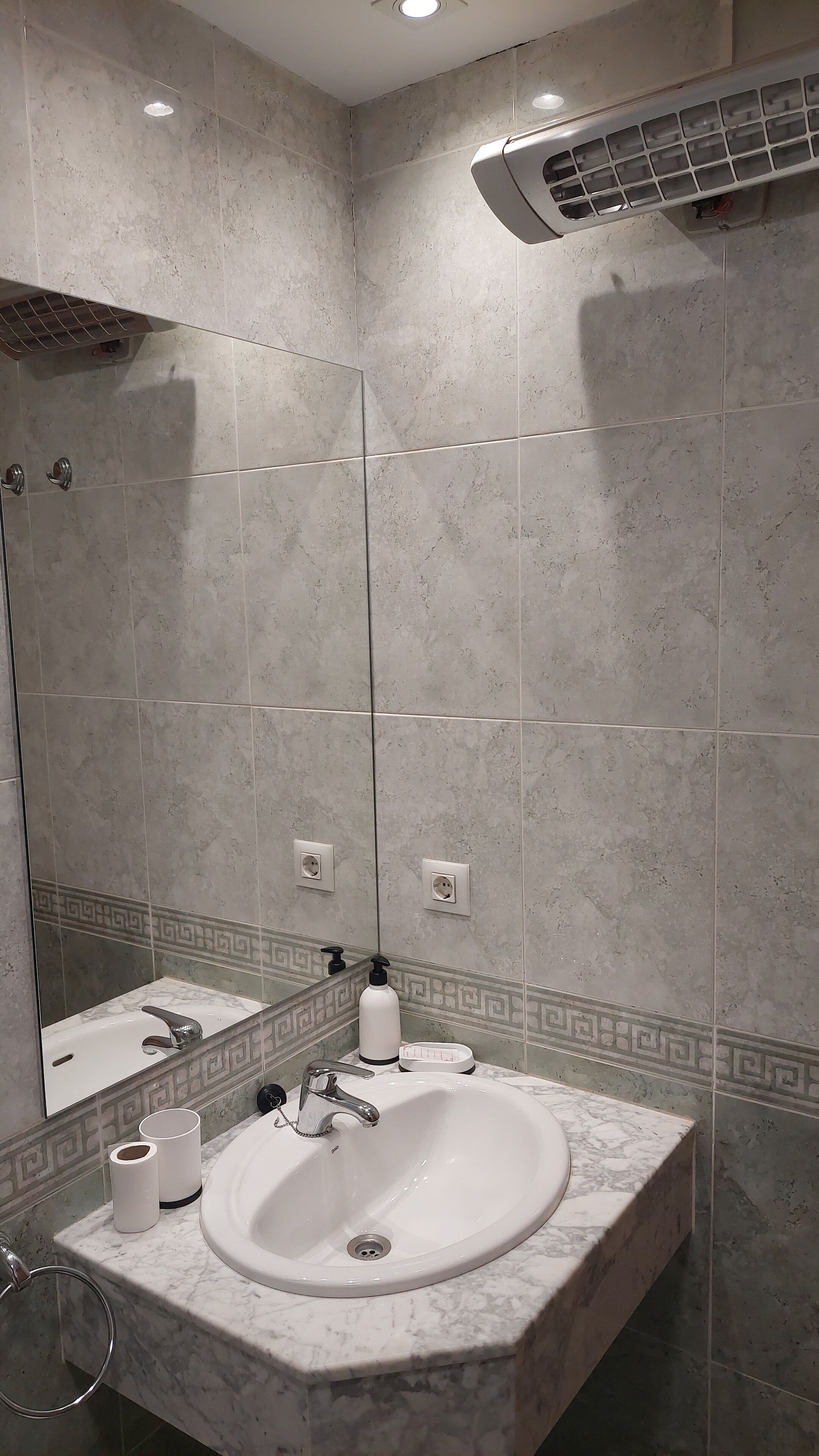 A bathroom with a marble sink, a mirror, a towel ring, a toilet paper roll, and a soap dispenser.