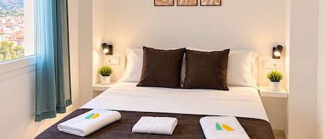 Una habitación de hotel con una cama grande, dos mesitas de noche, una lámpara colgante y una obra de arte en la pared.