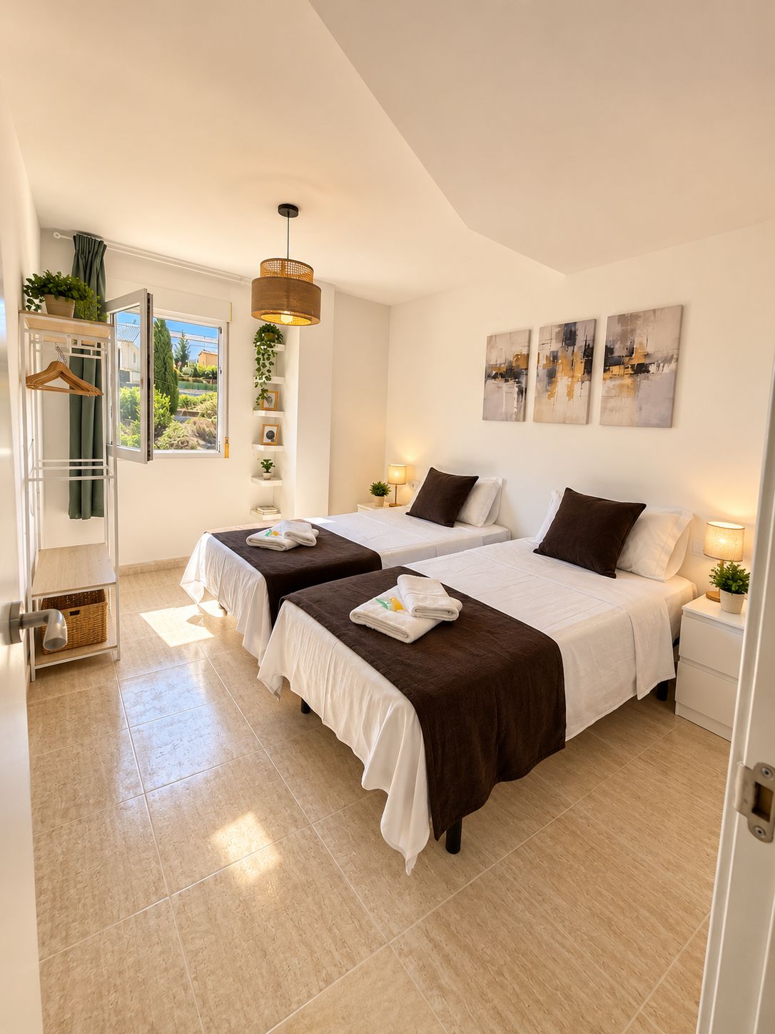 Habitación de hotel con dos camas, ventana con vistas, lámpara colgante y obras de arte en la pared.