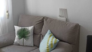 A living room with a grey sofa, two cushions, a small shelf with decorative items, and a wall-mounted air conditioner. - RESIDENCIAL ALCOY (Alcoy)