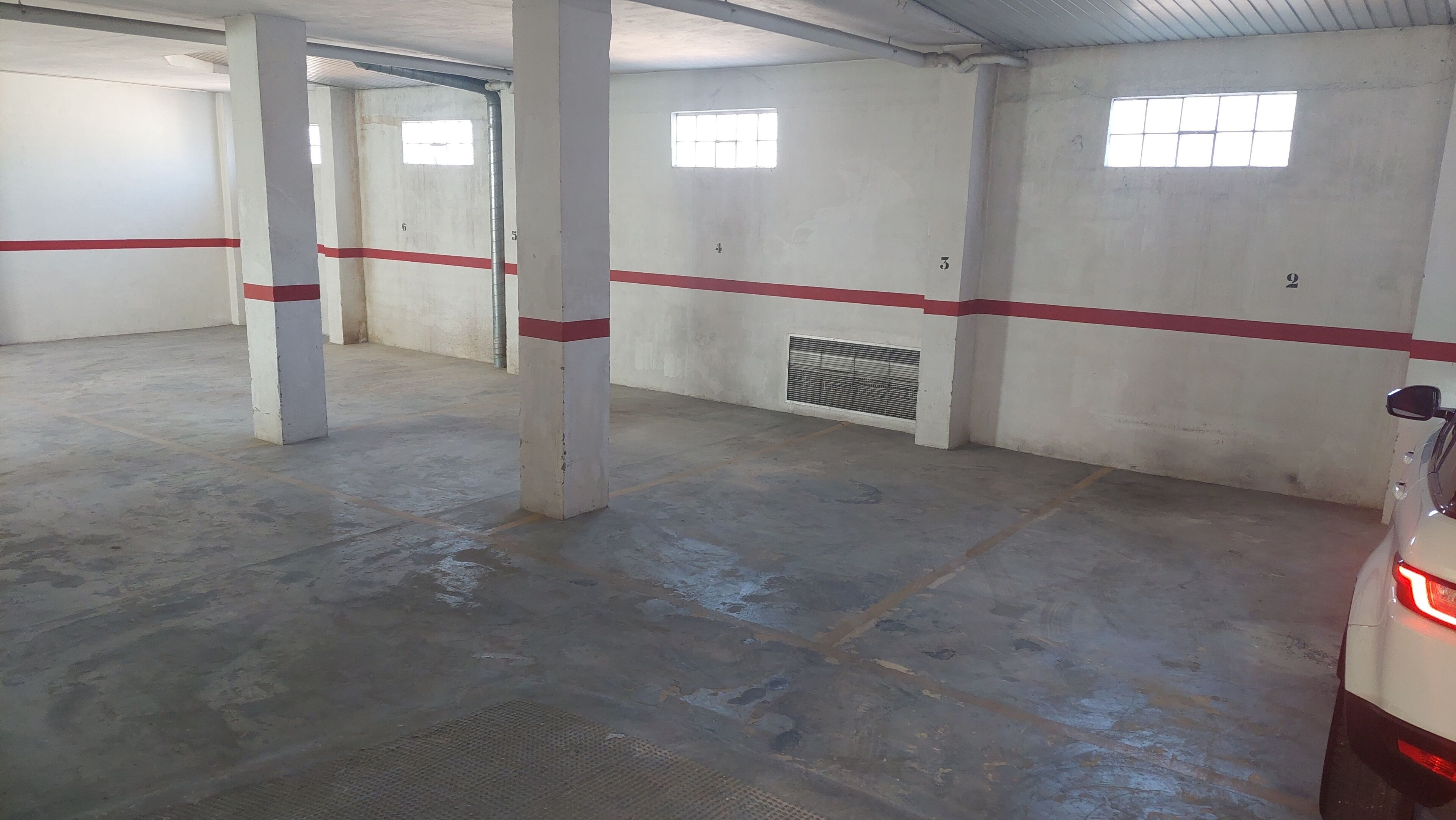 Eine Parkgarage mit Betonböden und -wänden, nummerierten Stellplätzen und Lüftungsgittern.