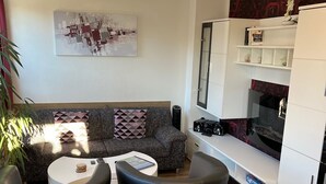 Un salon moderne comprenant un canapé, deux fauteuils noirs, une table basse et un meuble pour la télévision avec un téléviseur à écran plat.