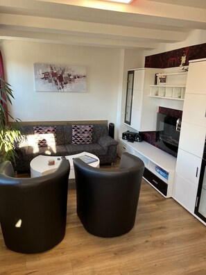 Een moderne woonkamer met een bank, twee zwarte fauteuils, een salontafel en een tv-meubel met een flatscreen televisie.