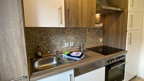 Une cuisine avec des meubles blancs et en bois, un évier en acier inoxydable, une cuisinière et un dosseret carrelé.