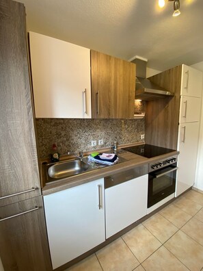 Een keuken met witte en houten kastjes, een roestvrijstalen spoelbak, een fornuis en een betegelde spatwand.