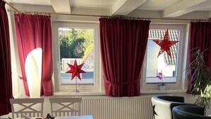 Une pièce comprenant une table à manger, des chaises, un radiateur et de grandes fenêtres avec des rideaux rouges.