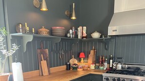 A kitchen with dark cabinetry, a gas stove, and a Viking oven. There are shelves with kitchenware and a red lamp on the countertop.