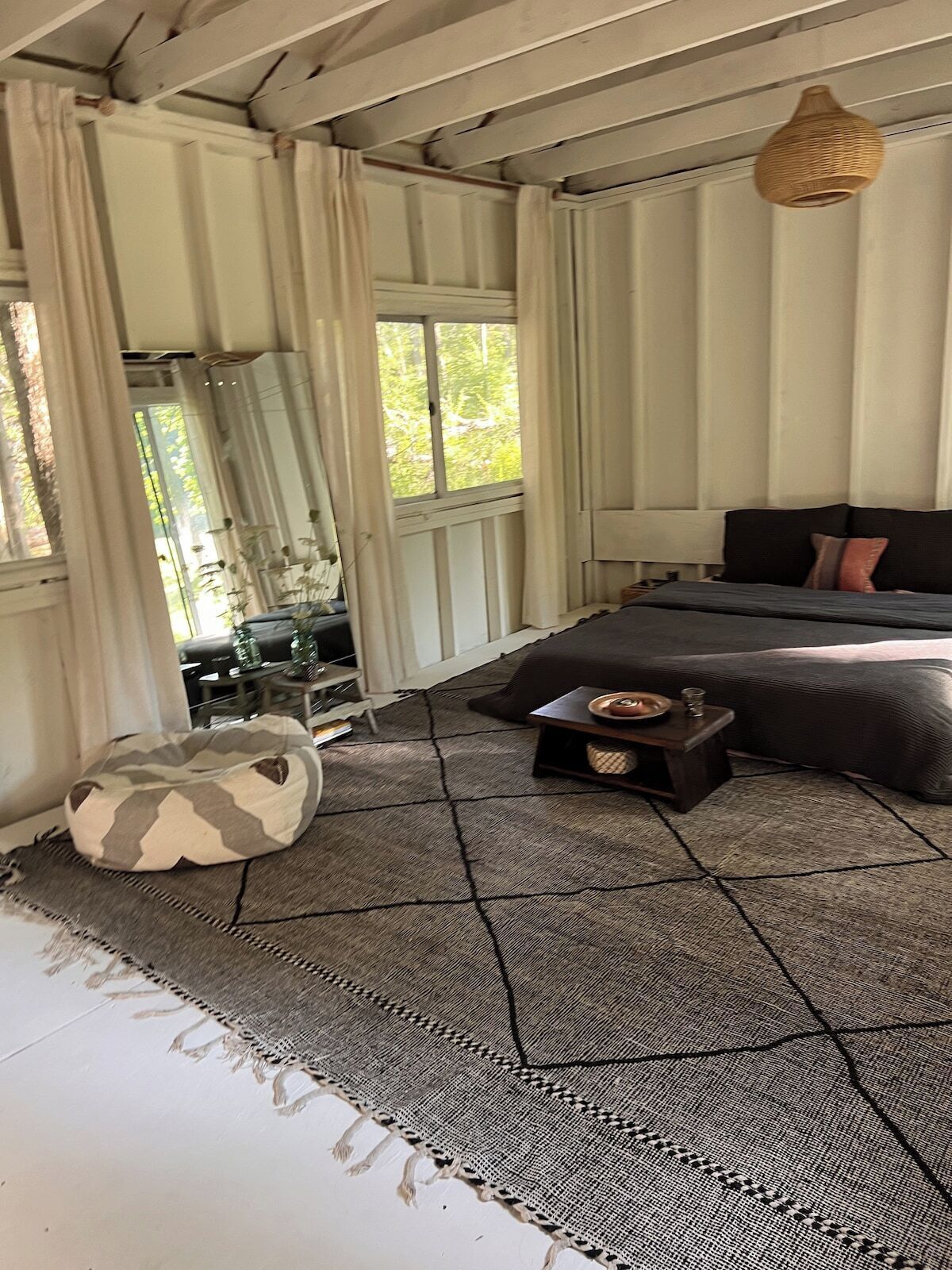 Um quarto com cama, uma mesa pequena, um pufe e um lustre.
