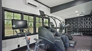 Et fitnessrum med løbebånd, crosstrainer og motionscykel. Der er et fjernsyn på et stativ og en vægmonteret aircondition.