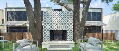 Un patio moderno al aire libre con una chimenea, rodeado de muebles blancos y árboles.
