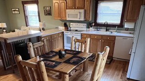 A wooden dining table with chairs, a kitchen with wooden cabinets, a microwave, and a refrigerator. - Serenity Gardens located in the Rolling Hills of Appalachia Ohio (Albany)