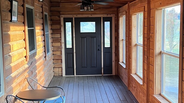 A log cabin with a wooden deck, a dining table with chairs, and a black door with windows. - Serenity Gardens located in the Rolling Hills of Appalachia Ohio (Albany)