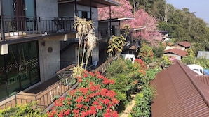 A multi-story building with balconies, surrounded by lush greenery and flowering plants. - Baan Rabiengfah resort (Wiang Kaen)