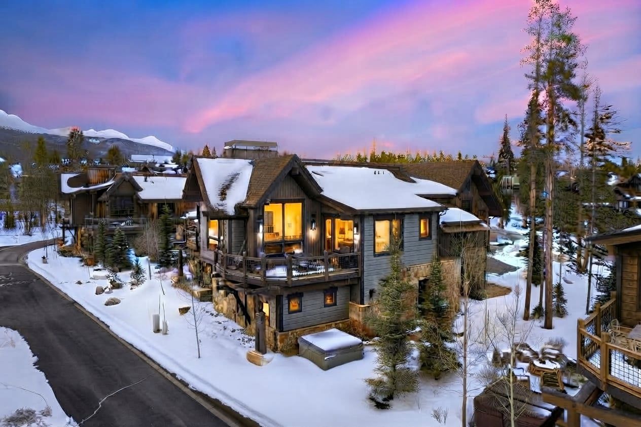 Ein großes Chalet mit mehreren Ebenen und einem Balkon, umgeben von schneebedeckten Bäumen und einem Bergpanorama.