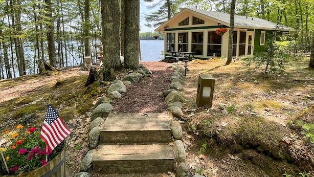 A cabin with a stone staircase leading to a dock, surrounded by trees and a lake.