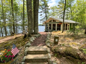 Une cabane avec un escalier en pierre menant à un quai, entourée d’arbres et bordée par un lac.