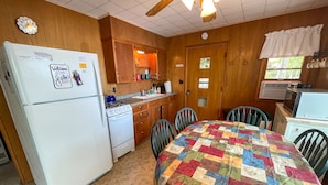 A compact kitchen with a refrigerator, stove, sink, and a dining table with chairs.