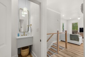 A modern bathroom with a large mirror, white vanity, and a wooden staircase leading to a balcony.