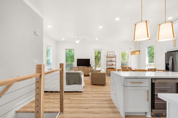 A modern interior with a kitchen, dining area, and living room, featuring wooden floors, white walls, and pendant lighting.
