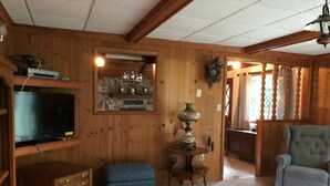 Una sala de estar acogedora con paredes de madera, un televisor, una chimenea, un otoman azul y un sillón gris.