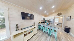Une cuisine moderne dotée d’un grand îlot central, de tabourets de bar et d’un téléviseur à écran plat fixé au mur.