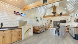 A spacious kitchen with wooden cabinets, a central island, and a dining area with a sofa and bar stools. - Welcome to our picturesque ranch oasis less than 1 hour from DFW!  (Cleburne)