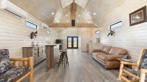 A spacious room with wooden walls, a high ceiling, and a central seating area with a leather couch and wooden chairs. - Welcome to our picturesque ranch oasis less than 1 hour from DFW!  (Cleburne)