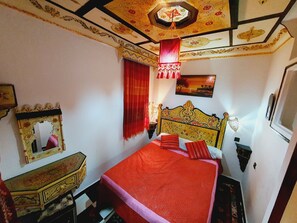Cozy retreat with a bed, wooden headboard, and decorative lamp, featuring a mirror and a small chest.
