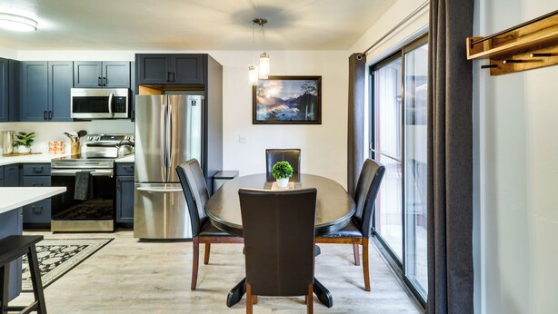 A modern kitchen with dark cabinets, stainless steel appliances, and a dining area with a round table and chairs. - Whitefish Condo w/ Pool Access + Close to Hiking! (Whitefish)