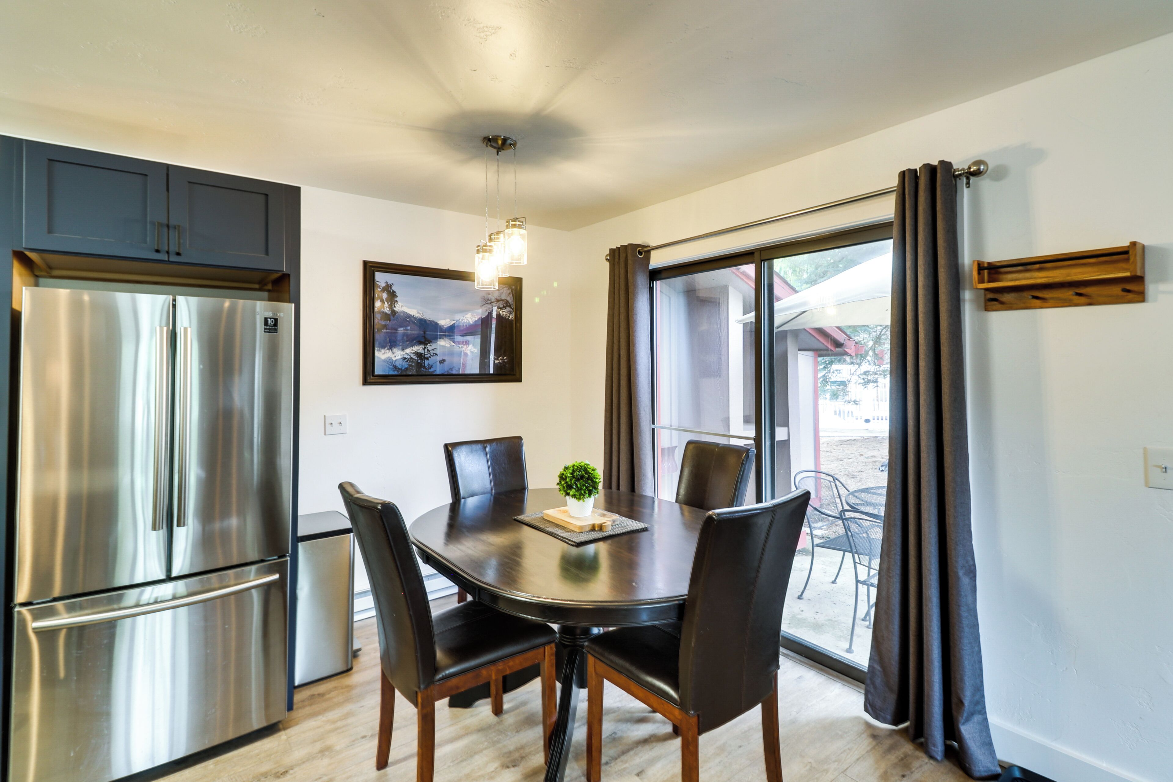 Una cocina moderna con un refrigerador de acero inoxidable, una mesa de comedor con sillas y vistas a través de un ventanal.