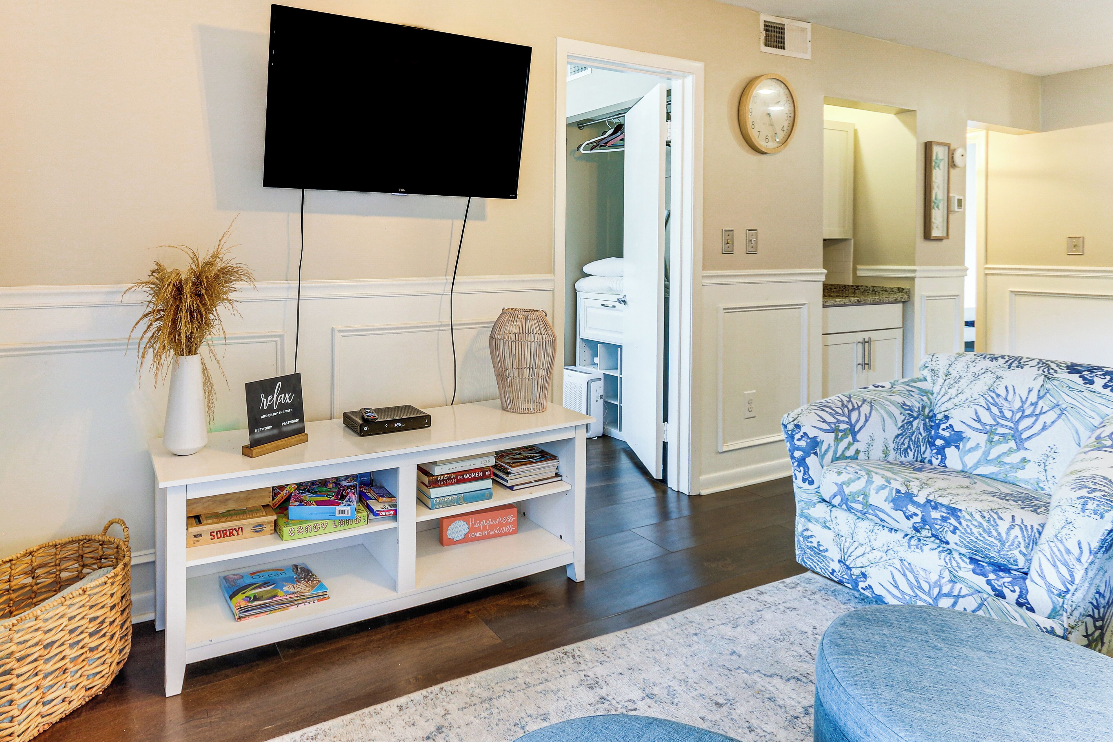 Una sala de estar con un mueble blanco para entretenimiento, un televisor de pantalla plana, un sofá azul con estampado y una cesta de mimbre.