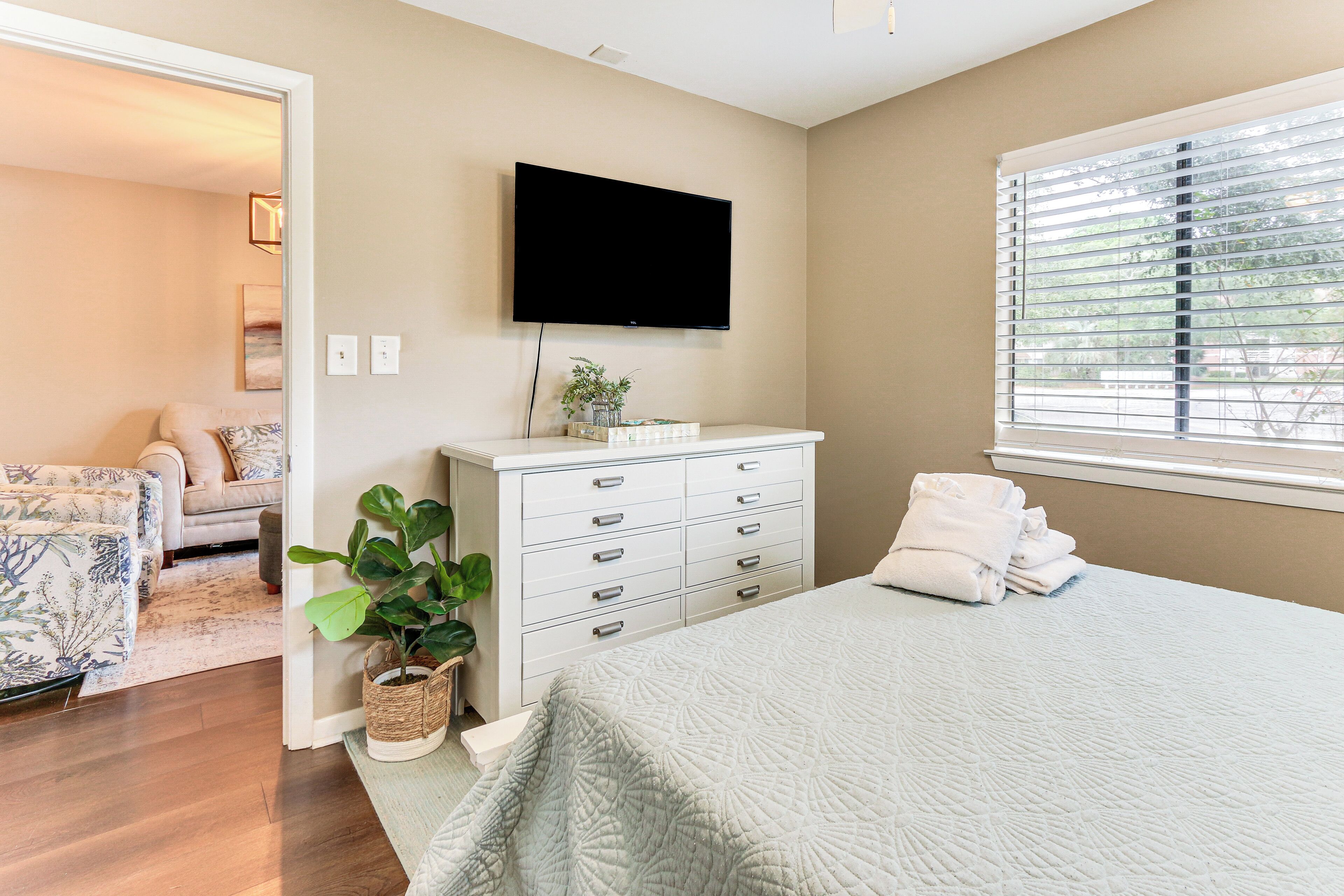 A bedroom with a bed, a dresser, a television, and a window with blinds.